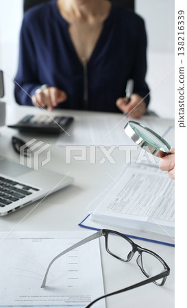 Two professional accountants or auditors reviewing financial reports and analyzing data using a calculator and a magnifying glass. Audit and taxes in business Two professional accountants or auditors reviewing financial reports and analyzing data using a calculator and a magnifying glass. Audit and taxes in business 138216339