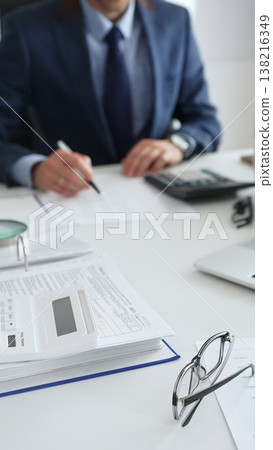 Close up of calculator while male accountant calculating taxes and analyzing financial data in office setting. Audit and taxes in business Close up of calculator while male accountant calculating taxes and analyzing financial data in office setting. Audit and taxes in business 138216349