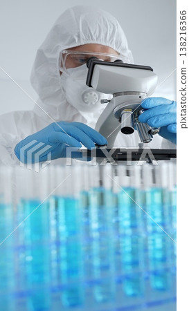 Scientific researcher wearing protective gear adjusting microscope, analyzing lab samples with precision opposite lab tubes in laboratory environment. Medicine, healthcare and science concept Scientific researcher wearing protective gear adjusting microscope, analyzing lab samples with precision opposite lab tubes in laboratory environment. Medicine, healthcare and science concept 138216366