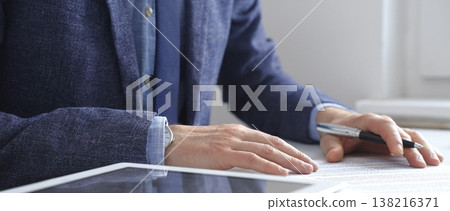 Professional businessman signing contract with silver pen, wearing tailored suit, business documents and digital tablet nearby. Business people concept Professional businessman signing contract with silver pen, wearing tailored suit, business documents and digital tablet nearby. Business people concept 138216371