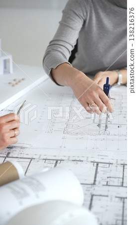 Architects discussing architectural blueprints and a building model on a white desk, planning a new construction project and developing innovative design solutions collaboratively, close up 138216376