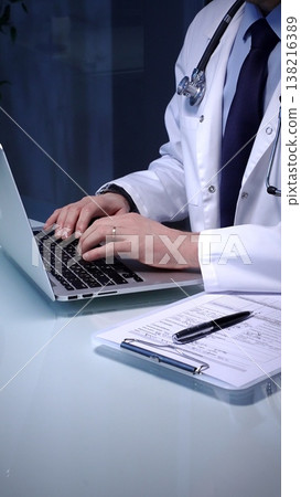 Medical doctor in lab coat with stethoscope typing on laptop in a dim office, managing electronic health records and telemedicine data for modern digital healthcare workflows Medical doctor in lab coat with stethoscope typing on laptop in a dim office, managing electronic health records and telemedicine data for modern digital healthcare workflows 138216389
