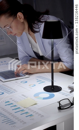 Businesswoman hands analyzing financial data and charts on a digital tablet at an office desk, surrounded by printed reports for marketing strategy and management Businesswoman hands analyzing financial data and charts on a digital tablet at an office desk, surrounded by printed reports for marketing strategy and management 138216446