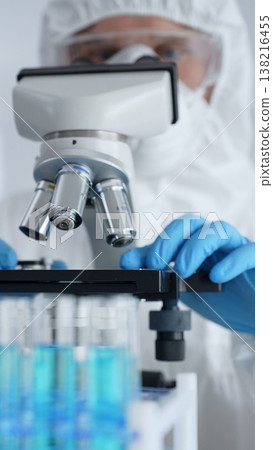Scientific researcher wearing protective gear adjusting microscope, analyzing lab samples with precision in sterile research environment. Medicine, healthcare and science concept Scientific researcher wearing protective gear adjusting microscope, analyzing lab samples with precision in sterile research environment. Medicine, healthcare and science concept 138216455