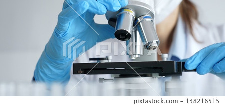Laboratory scientist wearing blue protective gloves carefully positioning microscope slide, demonstrating research precision. Medicine, healthcare and science concept Laboratory scientist wearing blue protective gloves carefully positioning microscope slide, demonstrating research precision. Medicine, healthcare and science concept 138216515