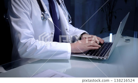 Medical doctor in lab coat with stethoscope typing on laptop in a dim office, managing electronic health records and telemedicine data for modern digital healthcare workflows Medical doctor in lab coat with stethoscope typing on laptop in a dim office, managing electronic health records and telemedicine data for modern digital healthcare workflows 138216524
