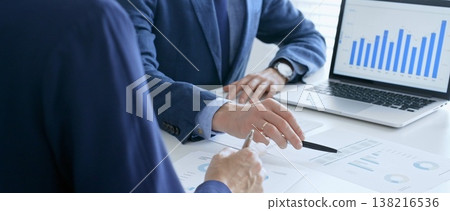 Business colleagues or partners are discussing financial data on a laptop and printed documents while analyzing charts and market trends at office table. Businesspeople and finance concept 138216536