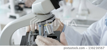 White gloved hands of scientist professional adjusting a microscope in a bright laboratory, emphasizing precision and focus in scientific research. Medicine, healthcare and science concept White gloved hands of scientist professional adjusting a microscope in a bright laboratory, emphasizing precision and focus in scientific research. Medicine, healthcare and science concept 138216567