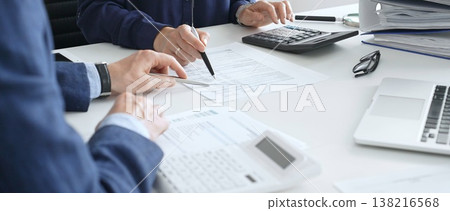 Business team analyzing financial documents, using calculators and laptop, working together on project in modern office. Audit and taxes concept Business team analyzing financial documents, using calculators and laptop, working together on project in modern office. Audit and taxes concept 138216568