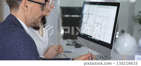 Architects discussing blueprints on computer monitor, collaborating on building design with hardhat and model. Business and architecture concept Architects discussing blueprints on computer monitor, collaborating on building design with hardhat and model. Business and architecture concept 138216633