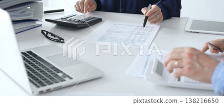 Female financial analysts with male colleague examining documents, using magnifying glass and calculator while examining corporate data at workplace in office. Audit and taxes in business Female financial analysts with male colleague examining documents, using magnifying glass and calculator while examining corporate data at workplace in office. Audit and taxes in business 138216650