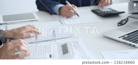Close up of female accountant hands using calculator while collaborating with male colleague in office, calculating taxes and analyzing financial data. Audit and taxes in business Close up of female accountant hands using calculator while collaborating with male colleague in office, calculating taxes and analyzing financial data. Audit and taxes in business 138216660