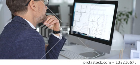 Architect discussing building blueprints on computer screen with colleague in modern office, managing engineering project. Business and architecture concept Architect discussing building blueprints on computer screen with colleague in modern office, managing engineering project. Business and architecture concept 138216673