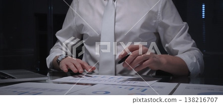 Business professional analyzing financial data with charts and reports on desk, working late in dark office. Audit and overworking concepts 138216707