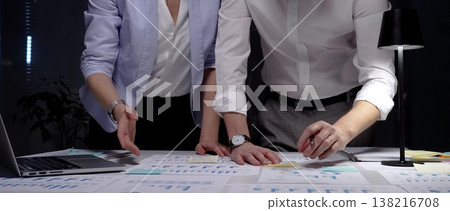 Business professionals collaborating on a data analysis project, reviewing financial reports and marketing strategies late in the evening to achieve corporate growth and success 138216708