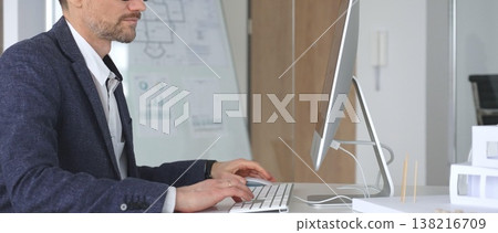 Architect working on computer in design office, planning and developing building projects with blueprints and models. Business and architecture concept 138216709