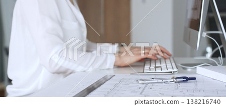 Architect creating new designs, working at a computer in office with blueprints and drafting tools. Business and architecture concept 138216740