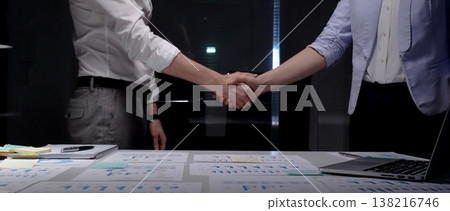 Business partners shaking hands over desk with financial documents, concluding deal, showing success in collaboration, partnership, and agreement during a late meeting at office Business partners shaking hands over desk with financial documents, concluding deal, showing success in collaboration, partnership, and agreement during a late meeting at office 138216746
