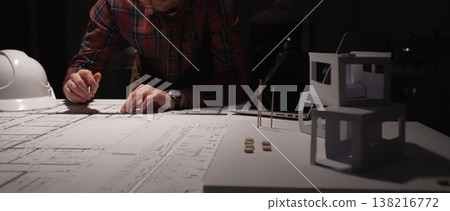 Female architect working late on detailed building blueprints using ruler and pencil, modern engineer designing construction plans at desk with laptop and hardhat Female architect working late on detailed building blueprints using ruler and pencil, modern engineer designing construction plans at desk with laptop and hardhat 138216772