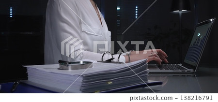Businesswomen working overtime in a dark office, typing on laptop with financial charts and data reports on desk at night. Audit and taxes in business Businesswomen working overtime in a dark office, typing on laptop with financial charts and data reports on desk at night. Audit and taxes in business 138216791