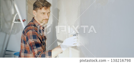 Male construction worker wearing protective gloves smoothing plaster onto wall surface during home renovation using professional trowel tool Male construction worker wearing protective gloves smoothing plaster onto wall surface during home renovation using professional trowel tool 138216798