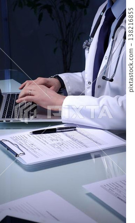 Medical doctor in lab coat with stethoscope typing on laptop in a dim office, managing electronic health records and telemedicine data for modern digital healthcare workflows Medical doctor in lab coat with stethoscope typing on laptop in a dim office, managing electronic health records and telemedicine data for modern digital healthcare workflows 138216855