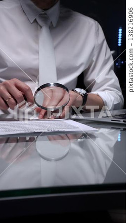 Business person examining a document using a magnifying glass, focusing on fine print and terms in a legal agreement, working late. Audit and overworking concepts 138216906