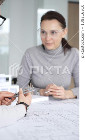 Architects collaborating on building project, discussing architectural model and blueprints on office table during creative planning and design session, close up 138216910