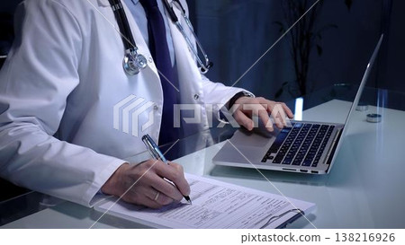 Medical professional wearing a white lab coat and stethoscope. Simultaneously typing patient data on a laptop keyboard and writing notes on a clipboard Medical professional wearing a white lab coat and stethoscope. Simultaneously typing patient data on a laptop keyboard and writing notes on a clipboard 138216926
