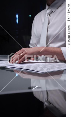 Man in white shirt reviewing legal documents, checking details of a contract with a magnifying glass on a dimly lit desk. Audit, business and overworking concepts 138216976