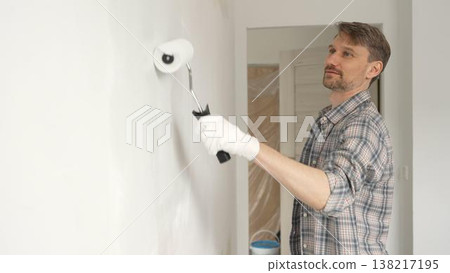 Middle aged man wearing checkered shirt, is rolling white paint on apartment wall with paint roller, transforming interior space with steady strokes during comprehensive home renovation Middle aged man wearing checkered shirt, is rolling white paint on apartment wall with paint roller, transforming interior space with steady strokes during comprehensive home renovation 138217195