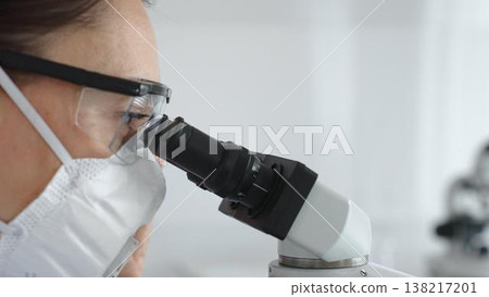 Female scientist peering into microscope, analyzing biological sample with precision in sterile laboratory research environment. Medicine and science concept Female scientist peering into microscope, analyzing biological sample with precision in sterile laboratory research environment. Medicine and science concept 138217201