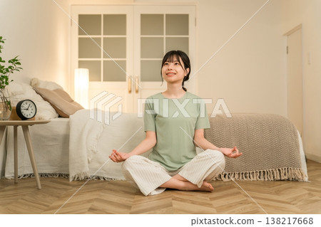 A young Asian woman doing yoga and meditation in her bedroom at night. 138217668