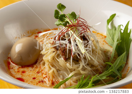 A rich and delicious oil-based noodle dish. It features a spicy soup, thin noodles, a soft-boiled egg, and vegetables as toppings. 138217883