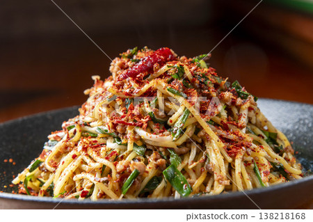 A spicy noodle dish topped with red chili peppers and green onions. A three-dimensional, Asian-style presentation of stir-fried noodles. A spicy noodle dish topped with red chili peppers and green onions. A three-dimensional, Asian-style presentation of stir-fried noodles. 138218168