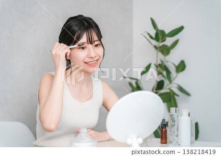 一位年輕的亞洲女性正在塗睫毛膏,打造眼妝。 一位年輕的亞洲女性正在塗睫毛膏,打造眼妝。 138218419