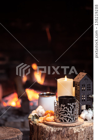 Cozy composition with a cup, candle and tangerines on a stump near the fireplace copy space. 138219288