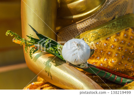Close up of lotus flower offering placed on golden Buddha statue hand in Thai temple 138219499