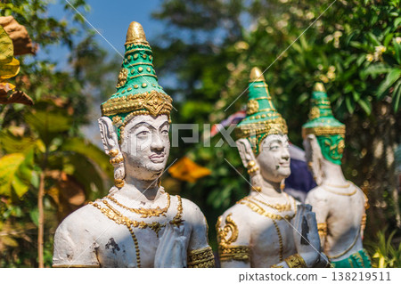 Traditional Thai Guardian Statues With Ornate Green And Gold Headdresses In Tropical Garden Traditional Thai Guardian Statues With Ornate Green And Gold Headdresses In Tropical Garden 138219511