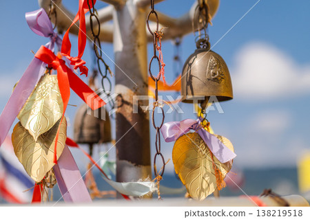 Hanging temple bells and golden leaf ornaments with colorful ribbons in Thai Buddhist shrine Hanging temple bells and golden leaf ornaments with colorful ribbons in Thai Buddhist shrine 138219518