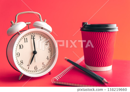 White alarm clock, paper cup and notepad on a blurred background. White alarm clock, paper cup and notepad on a blurred background. 138219660