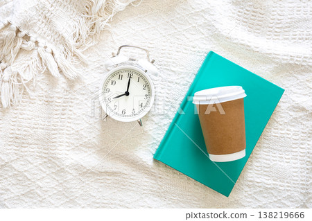 White alarm clock, paper disposable cup and green book in white bed, top view. White alarm clock, paper disposable cup and green book in white bed, top view. 138219666