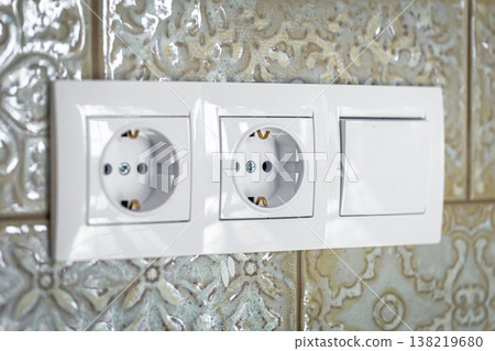 White plastic walk-through switches and sockets on a white wall. 138219680