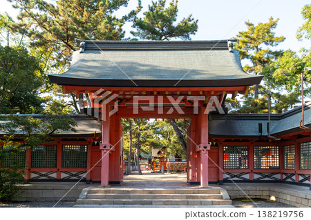 Grand red gate of a traditional Japanese Shinto shrine, surrounded by lush pine trees under a clear sky. A scene showcasing historical architecture and peaceful religious culture in Japan. 138219756
