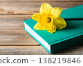 Yellow flower and book on a blurred wooden background, close-up. 138219846