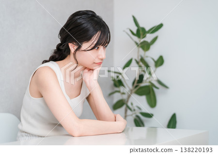 A young Asian woman in a tank top resting her chin on her hand and thinking 138220193