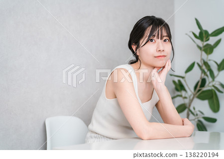 一位年輕的亞裔女子穿著背心，手托著下巴，若有所思。 138220194