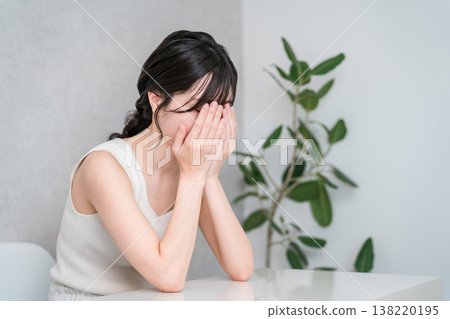 一位身穿背心的年輕亞裔女子哭泣，可能是因為壓力或驚嚇而感到擔憂。 138220195