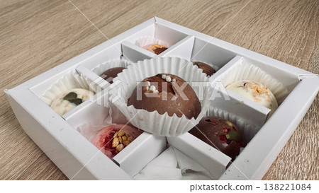 Delicious, sweet handmade chocolates made of white and milk chocolate with whole nuts in a gift box on a light background 138221084