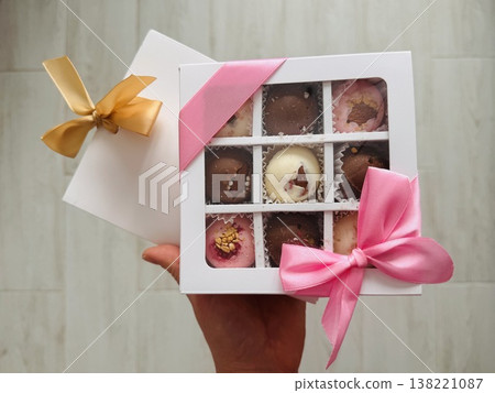 Delicious, sweet handmade chocolates made of white and milk chocolate with whole nuts in a gift box on a light background Delicious, sweet handmade chocolates made of white and milk chocolate with whole nuts in a gift box on a light background 138221087